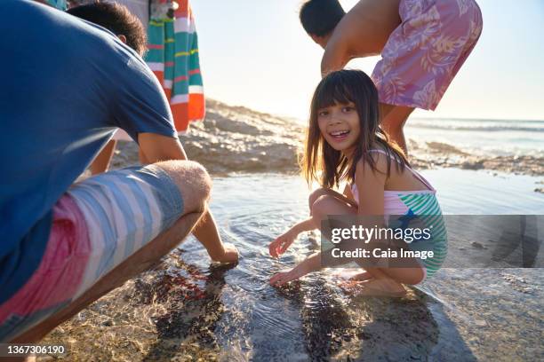 portrait happy girl playing in tide pool with family on sunny beach - gezeitentümpel stock-fotos und bilder