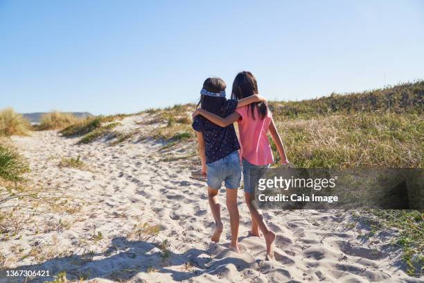 happy affectionate sisters walking on sunny beach - two girls brown hair stock pictures, royalty-free photos & images