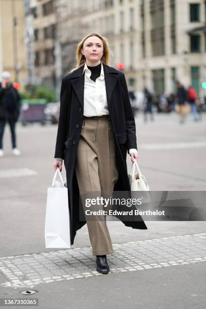 Guest wears a black turtleneck pullover, a white shirt, a black long coat, beige suit pants, a white leather handbag, black shiny leather block heels...