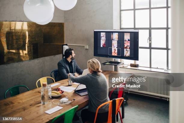 mature male and female entrepreneurs in video conference with colleagues during meeting at board room - remote location stock pictures, royalty-free photos & images