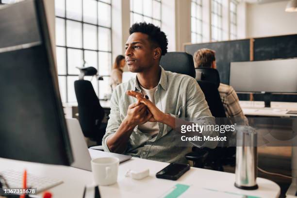 male employee applying sanitizer on hands while working with colleagues at office during pandemic - stockholm syndrome stock pictures, royalty-free photos & images