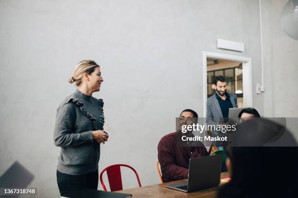 businesswoman discussing with male and female colleagues in board room at office - social distancing stockfoto's en -beelden