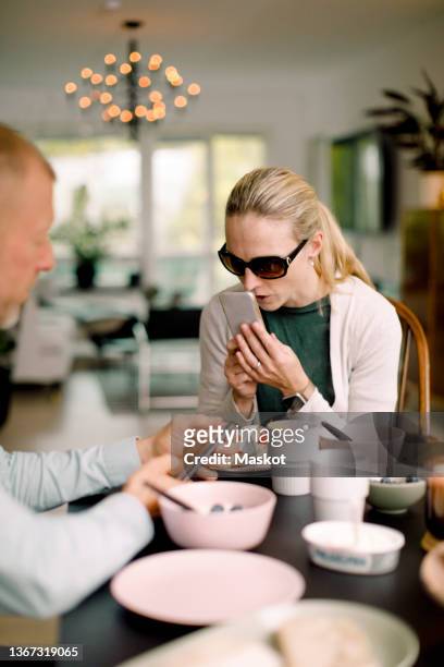 mature blind woman using voice commands through smart phone, sitting by man at home - speech recognition stock-fotos und bilder