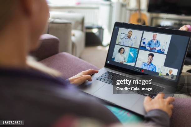 woman with laptop video chatting with doctors from sofa - doctor looking over shoulder stock pictures, royalty-free photos & images