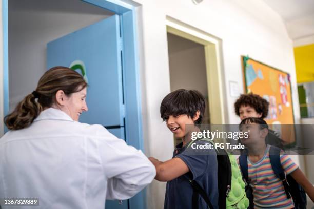 teacher greeting students with an elbow bump in the classroom - elbow bump stock pictures, royalty-free photos & images