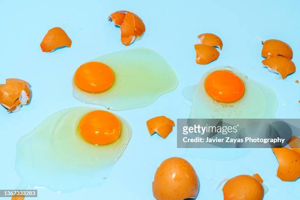 fresh broken eggs on a blue background - cracked egg stock-fotos und bilder