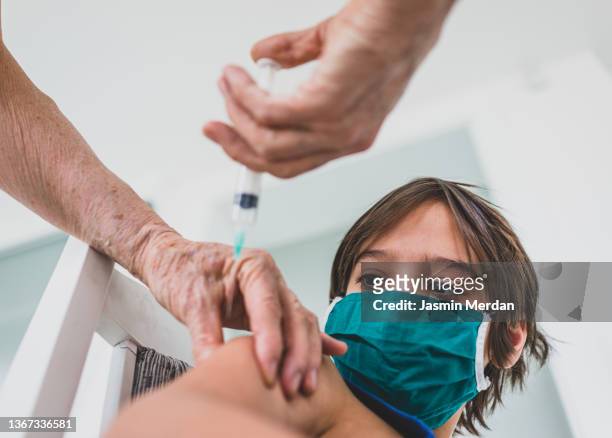 child wearing mask getting vaccinated by doctor holding a needle - 三種混合予防接種 ストックフォトと画像