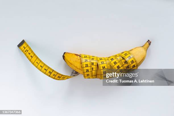 close-up of a measuring tape wrapped on a banana on a white leather background. - länge stock-fotos und bilder