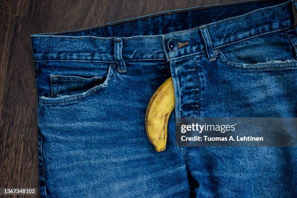 a banana coming out from fly of blue jeans as a flaccid penis. - disfunzione erettile foto e immagini stock