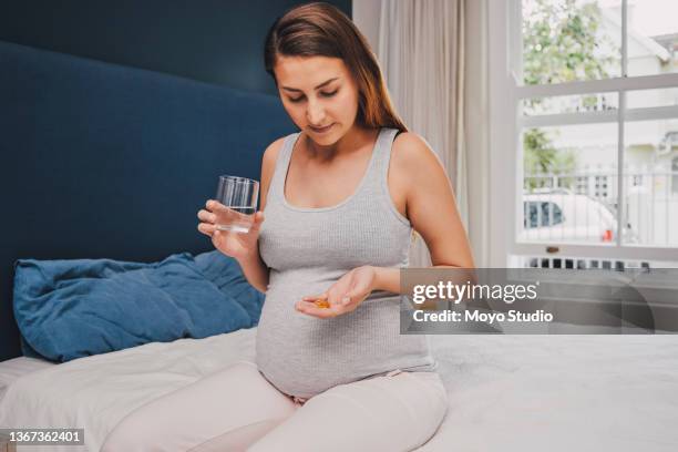 shot of a pregnant woman holding a glass of water and medication while sitting on her bed - tablet close up real copyspace stock pictures, royalty-free photos & images