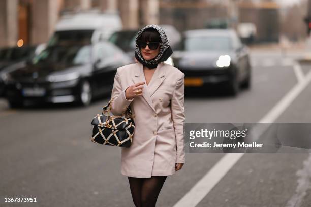 Gili Biegun wears a black with gray V monogram print pattern silk scarf from Valentino, black sunglasses, a beige blazer jacket dress, black tights,...