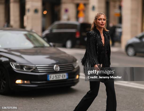 Maja Malnar wears large gold chain pendant earrings, a black shoulder-pad with embroidered sequins fringed jacket, a black silk with lace details...