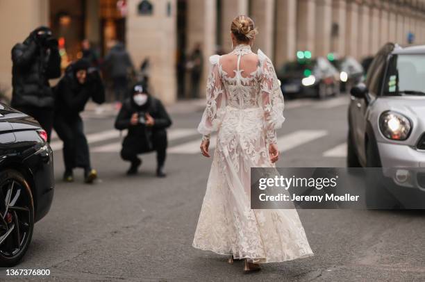 Veronica Ferraro wears a gold and diamond large pendant earrings, a white tulle and embroidered lace print pattern high neck / puffy sleeves / long...