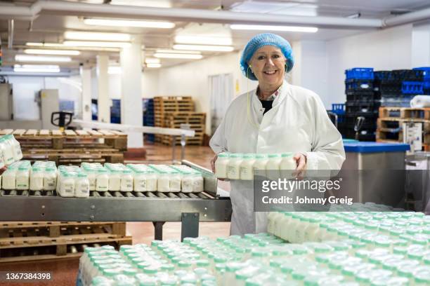 cheerful mid 60s woman working in milk bottling factory - femalefocuscollection stock-fotos und bilder