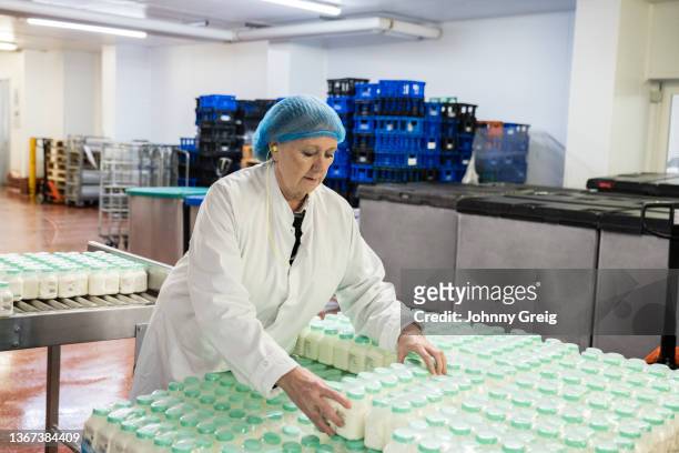 mid 60s woman stacking packaged milk containers - milk production line stock pictures, royalty-free photos & images