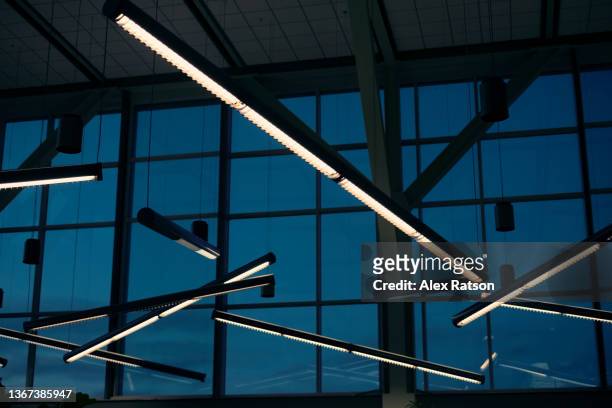 overhead florescent lights hangs from the sealing of a large airport terminal - fluorescent stock-fotos und bilder