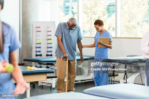 female therapist supports senior man walking with cane - showing empathy stock pictures, royalty-free photos & images