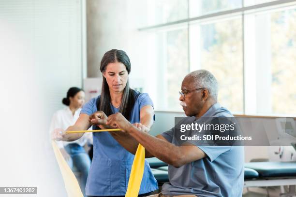 physiotherapeut für mittlere erwachsene unterrichtet elastische bandübungen für ältere männer - occupational therapist stock-fotos und bilder