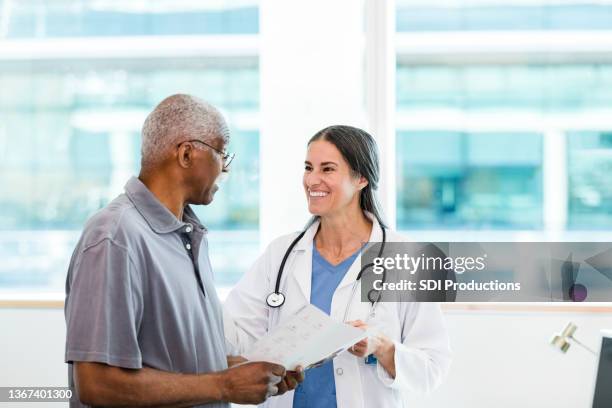 female surgeon smiles at senior patient holding brochure - surgeon patient stock pictures, royalty-free photos & images