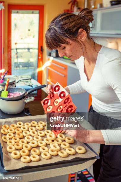 woman in domestic kitchen taking baked donuts from the oven - molding a shape stockfoto's en -beelden