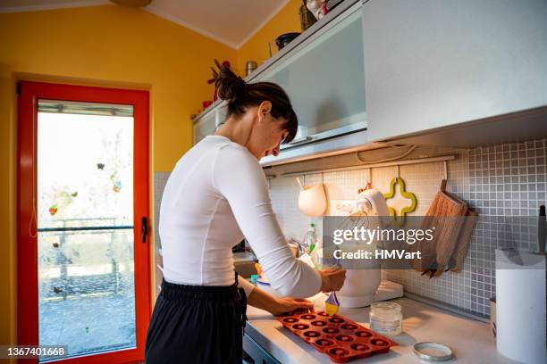 woman pouring the dough into small silicone donuts molds - silikone stock pictures, royalty-free photos & images