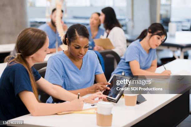 two female medical students use digital tablet to complete assignment - fisiologia imagens e fotografias de stock