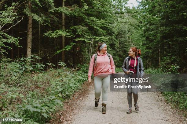 two female friends talking while hiking in the forest - two people hiking stock pictures, royalty-free photos & images