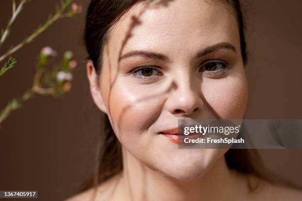 portrait of a beautiful caucasian overweight woman with a flower branch casting a shadow over her face - beautiful fat ladies stockfoto's en -beelden