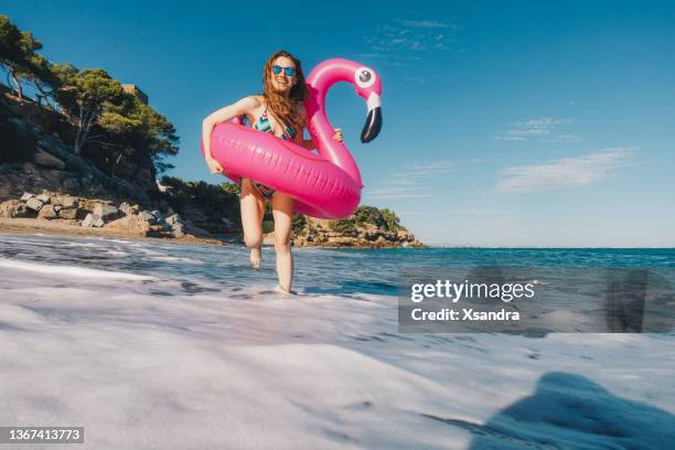 happy young woman with inflatable flamingo enjoying the sunny day at the beach - tubing stock pictures, royalty-free photos & images
