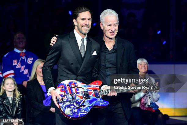 Former New York Ranger Henrik Lundqvist is presented with a gift by former tennis player John McEnroe during his jersey retirement ceremony prior to...