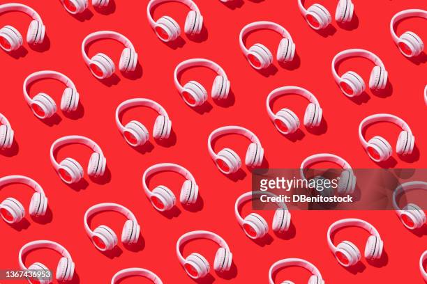 pattern of white wireless headphones with hard shadow on red background. concept of music, earphones, radio, podcast, listening and relaxing activity. - headphones fotografías e imágenes de stock