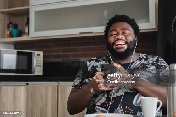 smiling, wearing her headset, young woman uses her cell phone - vitiligo stock pictures, royalty-free photos & images