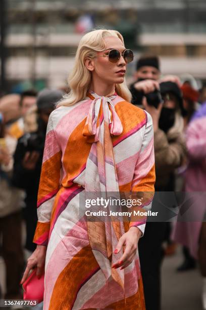Miss Fame wears sunglasses from Loewe, a white / pale pink / orange / fuchsia stripped print pattern long flowing dress from Fendi, a gold belt, a...