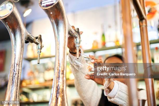 black woman pouring a glass of tap beer. - bier brouwen stockfoto's en -beelden