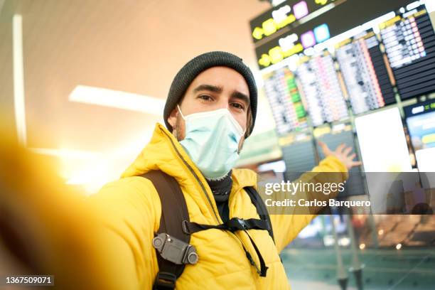 handsome caucasian man taking a selfie with the mask on at the airport. - departure board front on fotografías e imágenes de stock