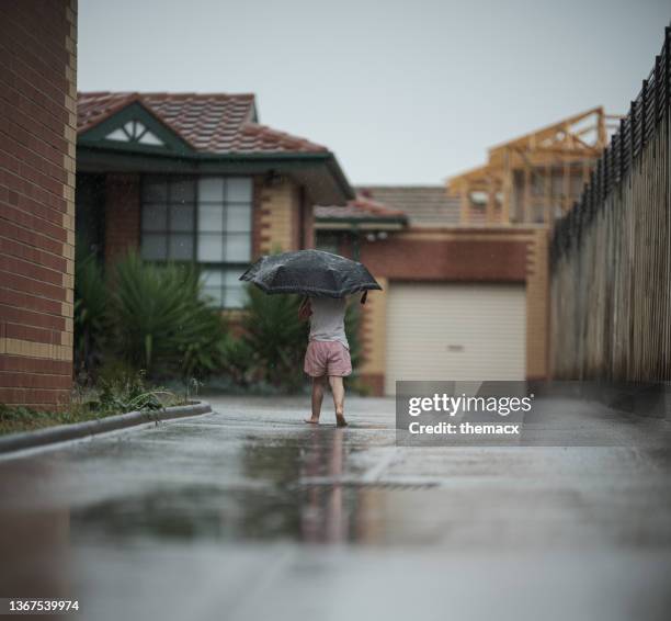 kleines mädchen, das spaß hat, mit dem regen mit regenschirm zu spielen - rainy season stock-fotos und bilder