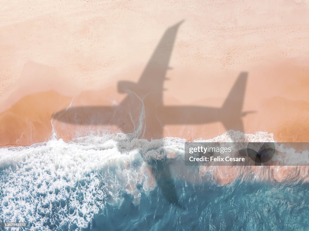 Aerial view of an airplane shadow over a sandy beach.