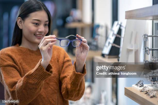 female holding eyeglasses at the optical store, choosing new pair of glasses in an optician shop. - lesebrille stock-fotos und bilder