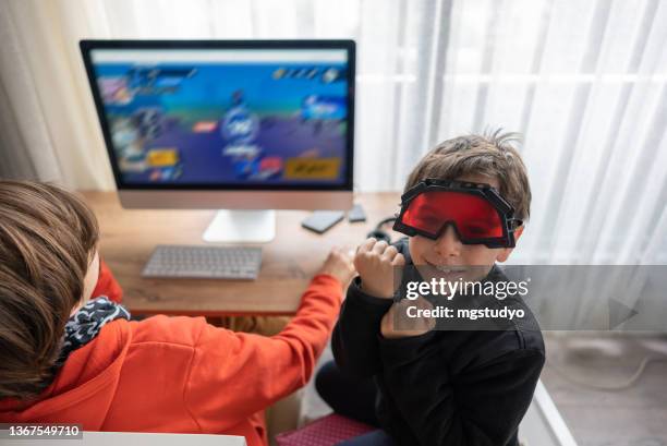garçon heureux jouant à un jeu vidéo à la maison avec son frère regardant la caméra. - lunettes 3d photos et images de collection