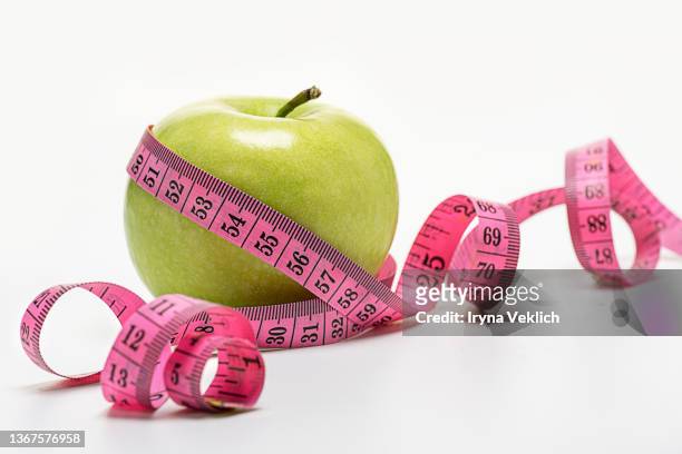 measuring tape wrapped around a green apple against white color background. - mass unit of measurement stock-fotos und bilder