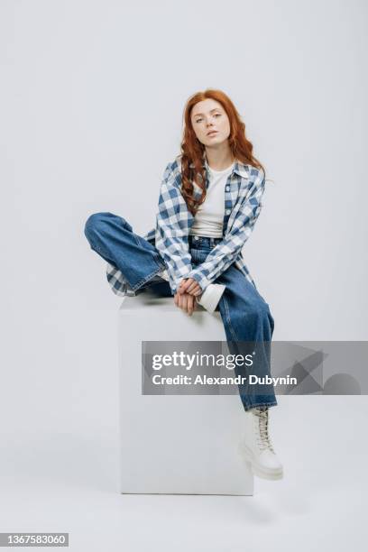 beautiful young model posing sitting in studio on cube white background casual new clothes catalog. fashion and trend concept - woman wearing white jeans stock-fotos und bilder