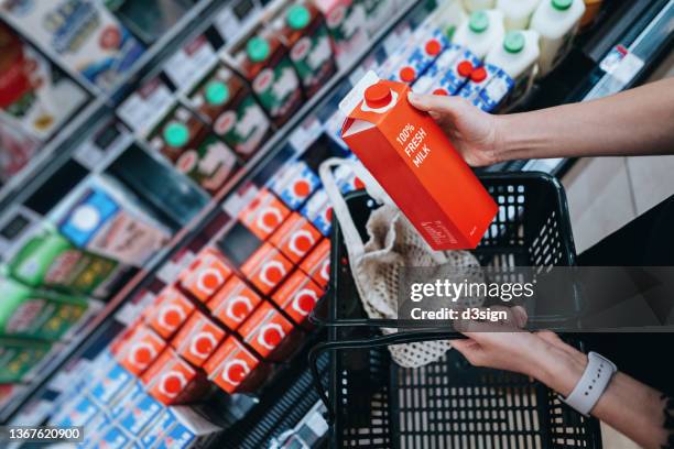 high angle view, close up hands of young asian woman grocery shopping for dairy product in supermarket. she is putting a carton of fresh milk into a cotton mesh eco bag in a shopping basket. environmentally friendly and zero waste concept - cesta de compras - fotografias e filmes do acervo