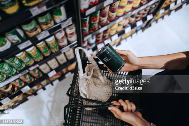 high angle view, close up hands of young asian woman grocery shopping in supermarket. she is putting a tin can into a cotton mesh eco bag in a shopping basket. environmentally friendly and zero waste concept - travée photos et images de collection