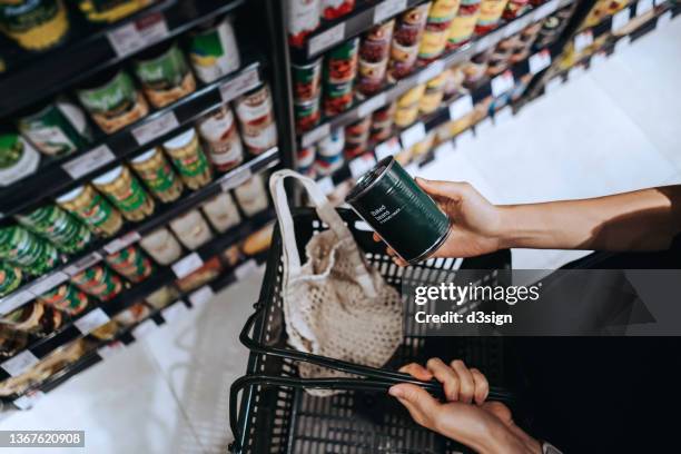 high angle view, close up hands of young asian woman grocery shopping in supermarket. she is putting a tin can into a cotton mesh eco bag in a shopping basket. environmentally friendly and zero waste concept - nutrition label stock pictures, royalty-free photos & images