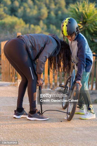 son wearing bicycle helmet looking at mother inflating bicycle tire while standing in the yard - inflating ストックフォトと画像