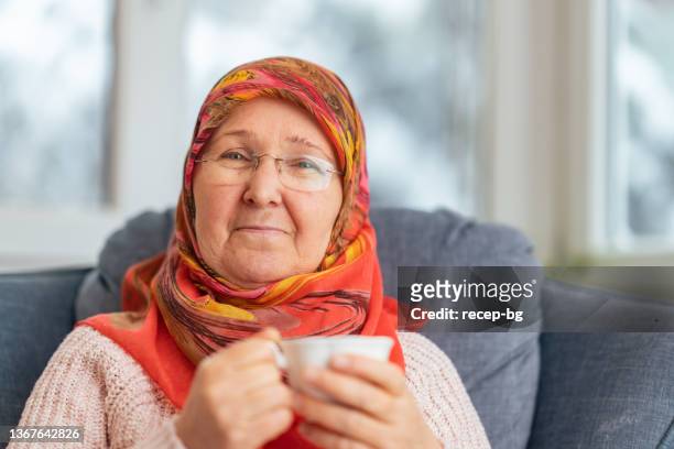 porträt einer muslimischen frau, die sich zu hause entspannt - arab old woman stock-fotos und bilder