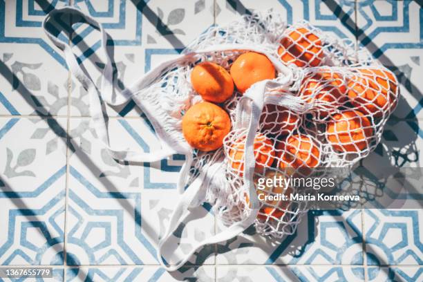 mesh shopping bag with fruit. tangerine . - frugalidad fotografías e imágenes de stock