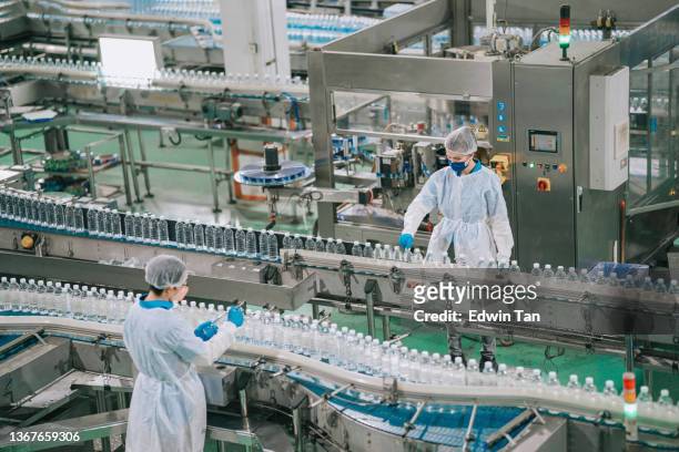 2 asian chinese drinking water factory production line workers with ppe examining water bottle working in daily routine - food and drink industry stock pictures, royalty-free photos & images