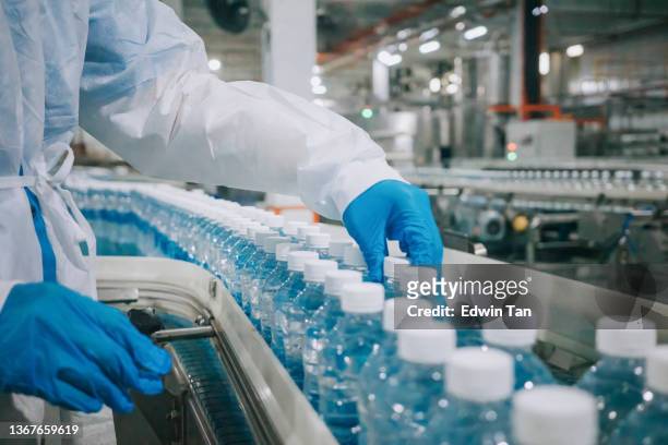 close up female asian chinese drinking water factory production line worker with ppe examining water bottle working in daily routine - surgical glove stock pictures, royalty-free photos & images