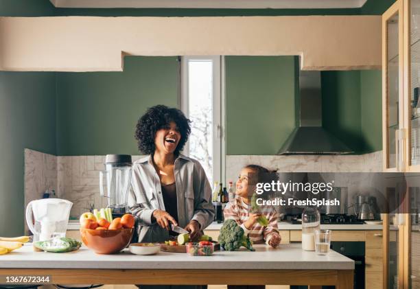 une mère célibataire afro-américaine préparant un déjeuner végétalien dans la cuisine et souriant avec sa petite fille - black room photos et images de collection